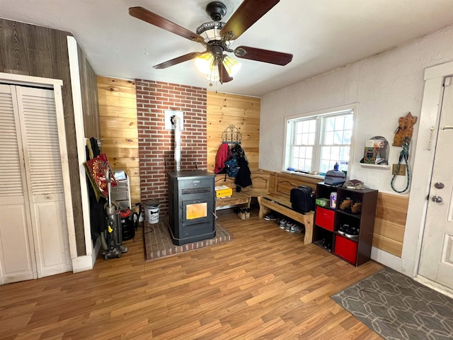 interior space featuring ceiling fan, wood walls, light wood-type flooring, and a wood stove