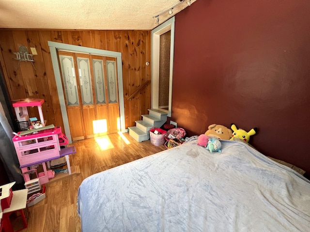 bedroom with a textured ceiling, wooden walls, hardwood / wood-style floors, a closet, and lofted ceiling