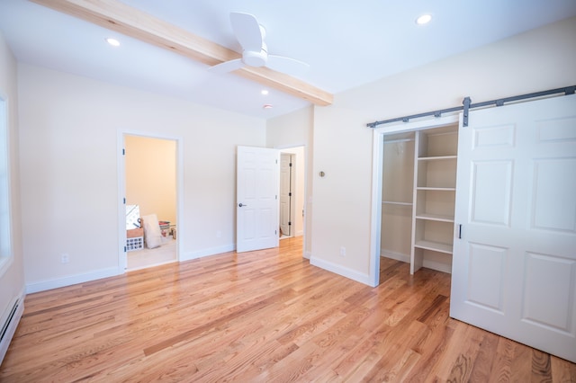 unfurnished bedroom with ensuite bathroom, ceiling fan, a baseboard heating unit, a barn door, and light hardwood / wood-style floors