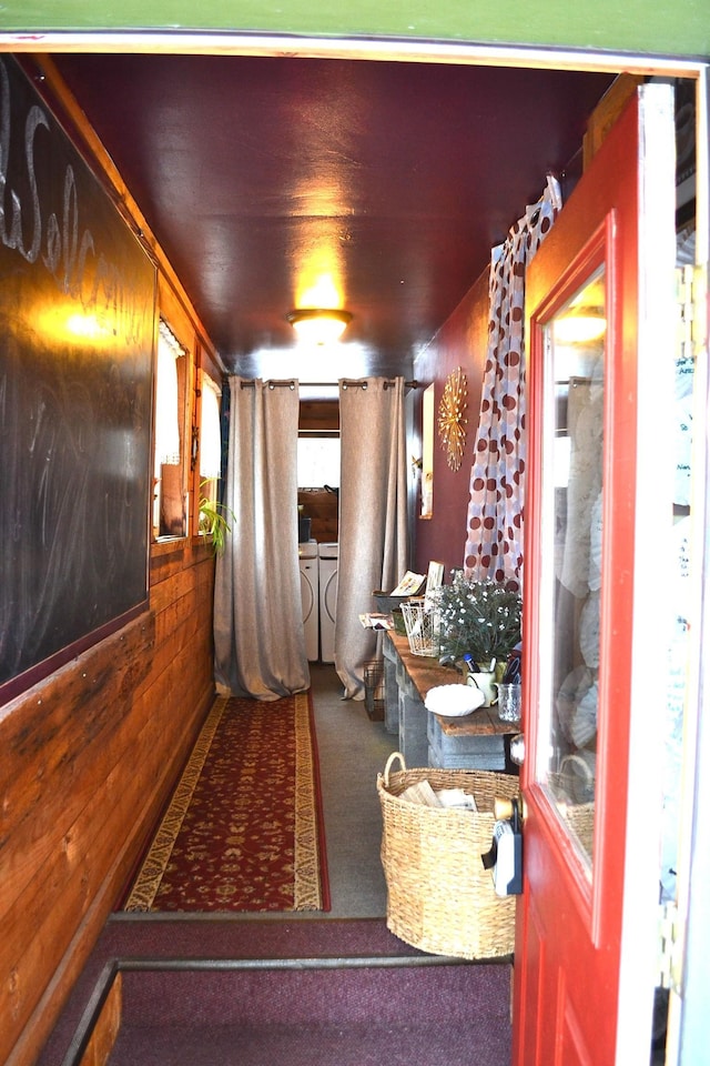 hallway with carpet flooring, wood walls, and independent washer and dryer