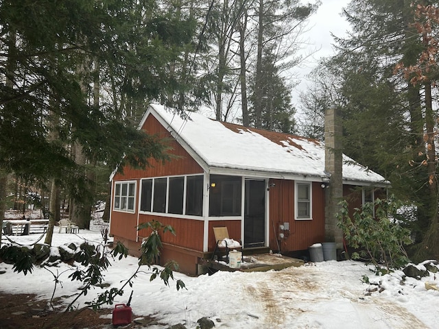 snow covered back of property featuring a sunroom