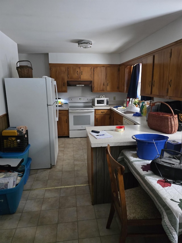 kitchen featuring white appliances, kitchen peninsula, light tile patterned floors, and a breakfast bar area