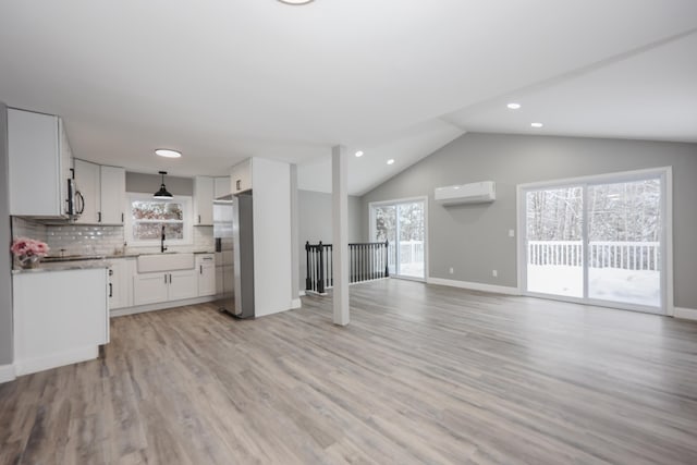 kitchen featuring light wood-type flooring, a wall mounted AC, decorative light fixtures, white cabinetry, and stainless steel appliances