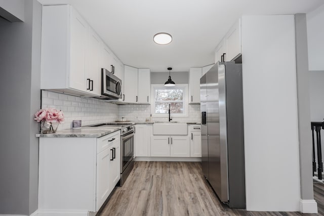 kitchen featuring sink, hanging light fixtures, stainless steel appliances, light hardwood / wood-style flooring, and white cabinets