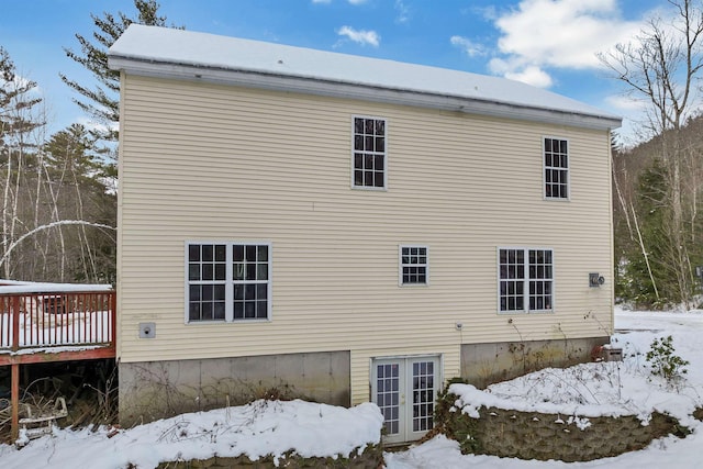 snow covered rear of property with a wooden deck and french doors