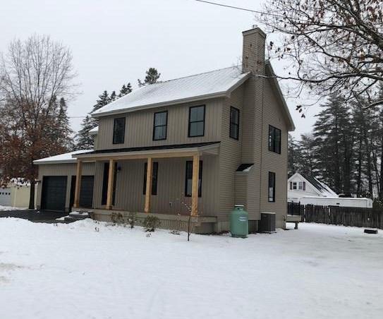 snow covered property featuring a porch, a garage, and cooling unit