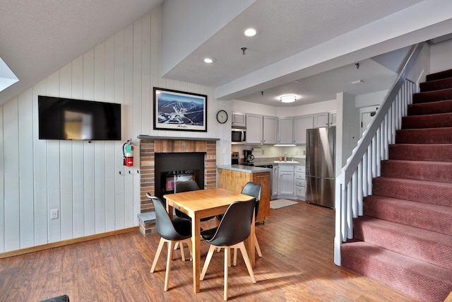 dining space featuring a brick fireplace, a textured ceiling, wooden walls, and light hardwood / wood-style flooring