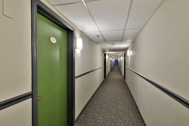 corridor featuring dark carpet and a drop ceiling