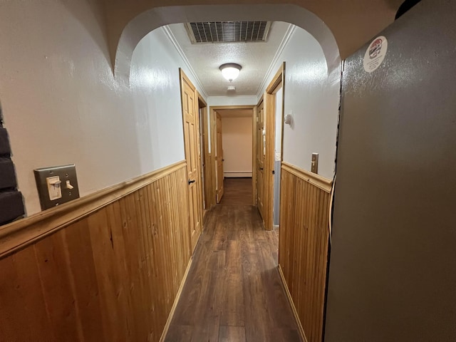 corridor featuring baseboard heating, wooden walls, crown molding, and dark wood-type flooring