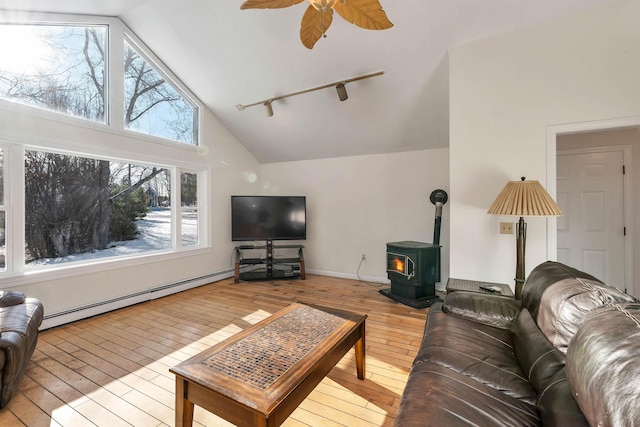 living room featuring a wood stove, ceiling fan, a baseboard radiator, light hardwood / wood-style flooring, and high vaulted ceiling