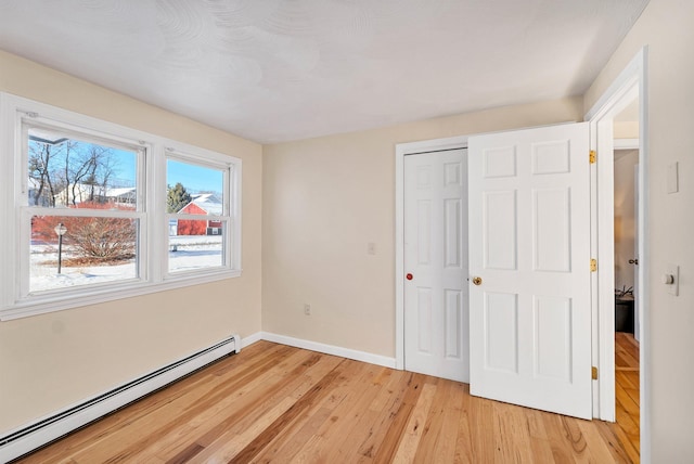 unfurnished bedroom with a closet, light hardwood / wood-style flooring, and a baseboard heating unit