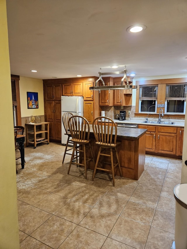 kitchen with sink, white fridge, pendant lighting, a breakfast bar area, and a kitchen island