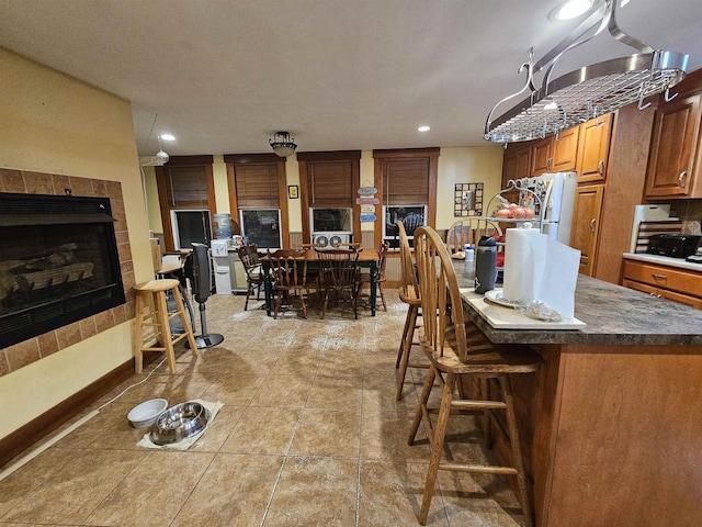 interior space with a tile fireplace, a kitchen island, light tile patterned floors, white fridge, and a kitchen bar