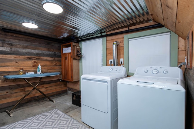 clothes washing area with washing machine and dryer and wood walls