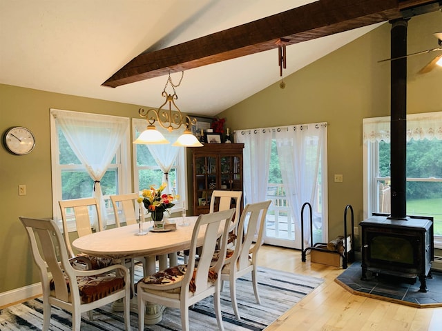 dining space featuring a wood stove, wood-type flooring, ceiling fan with notable chandelier, and vaulted ceiling with beams