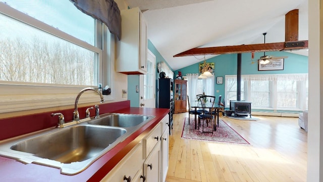 kitchen with a wood stove, white cabinetry, sink, and light wood-type flooring