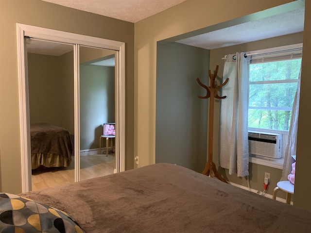 unfurnished bedroom featuring a textured ceiling, cooling unit, light hardwood / wood-style flooring, and a closet