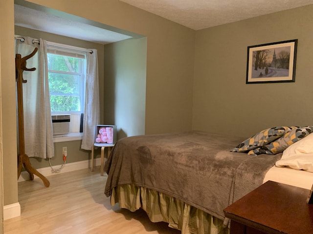 bedroom with cooling unit, light wood-type flooring, and a textured ceiling