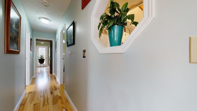 corridor with light hardwood / wood-style floors and a textured ceiling