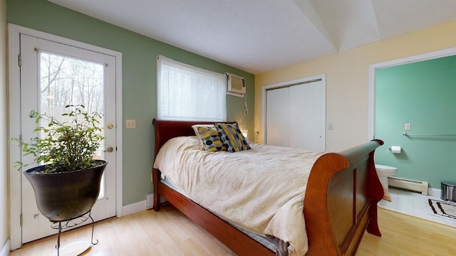 bedroom with light wood-type flooring, a wall mounted AC, and a baseboard heating unit