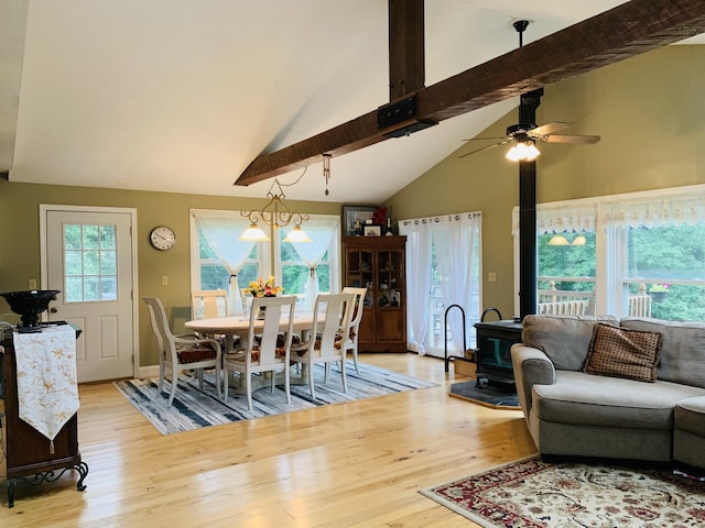 dining area featuring light wood-type flooring, vaulted ceiling with beams, a wood stove, and ceiling fan with notable chandelier