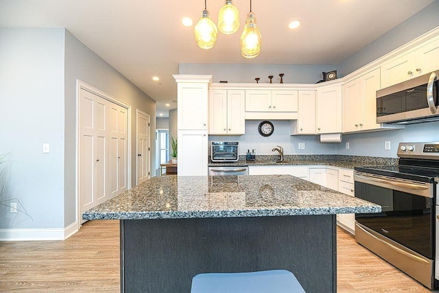 kitchen with a center island, hanging light fixtures, light hardwood / wood-style flooring, white cabinetry, and stainless steel appliances