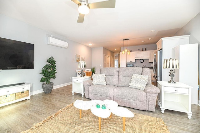 living room with a wall mounted AC, ceiling fan, and light hardwood / wood-style floors