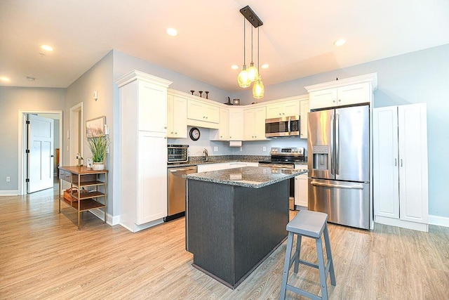 kitchen with light wood-type flooring, stainless steel appliances, decorative light fixtures, dark stone countertops, and a kitchen island