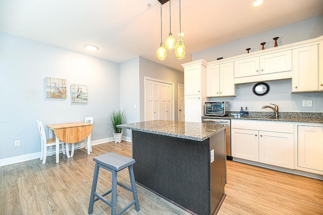 kitchen with white cabinets, dark stone countertops, light wood-type flooring, decorative light fixtures, and a kitchen island