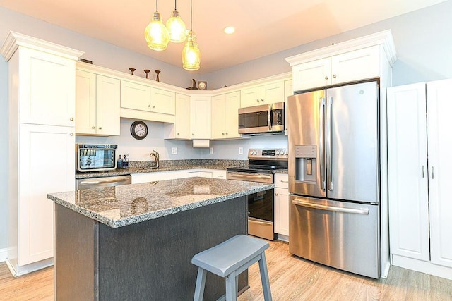 kitchen featuring a center island, stainless steel appliances, dark stone counters, decorative light fixtures, and light wood-type flooring