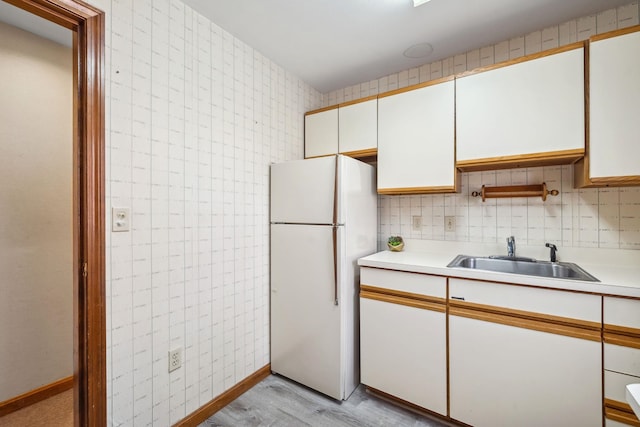 kitchen with light wood-type flooring, white refrigerator, white cabinetry, and sink