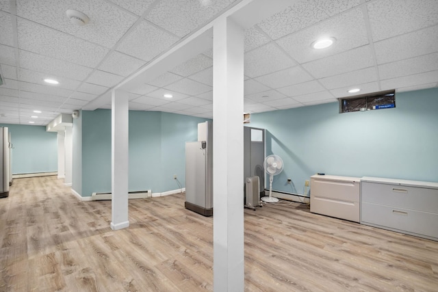 basement featuring a drop ceiling, light wood-type flooring, and baseboard heating