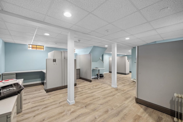 basement with radiator, light hardwood / wood-style flooring, and a drop ceiling