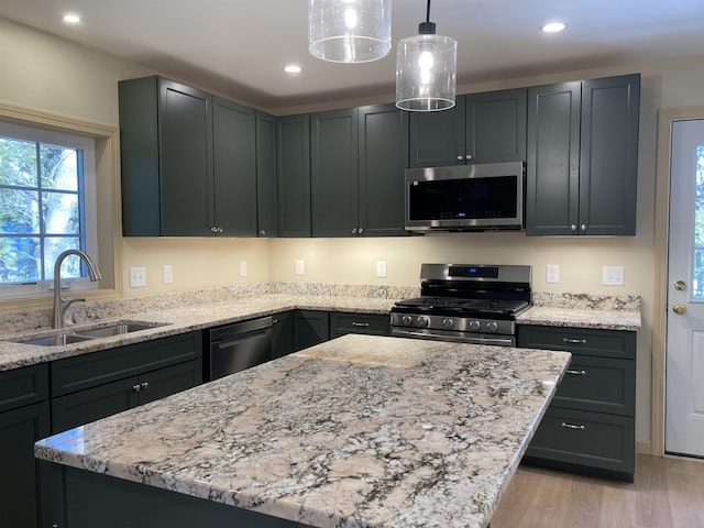 kitchen featuring sink, hanging light fixtures, stainless steel appliances, light hardwood / wood-style flooring, and a kitchen island