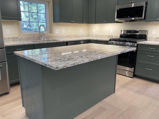 kitchen with a center island, sink, light wood-type flooring, light stone counters, and stainless steel appliances