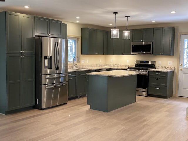 kitchen with a kitchen island, stainless steel appliances, hanging light fixtures, and light hardwood / wood-style flooring