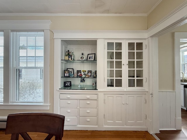 bar with wood-type flooring, white cabinetry, a baseboard heating unit, and ornamental molding