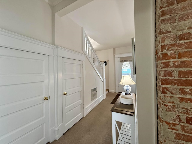 hallway with brick wall and dark colored carpet