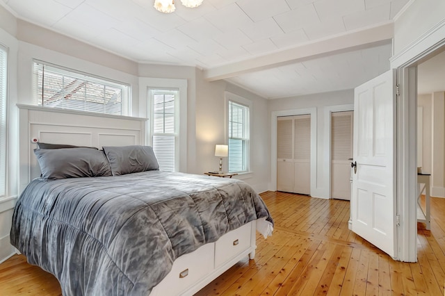 bedroom with two closets, light hardwood / wood-style floors, beam ceiling, and multiple windows