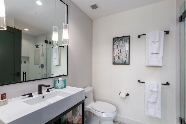 bathroom with toilet, a shower with shower door, and sink