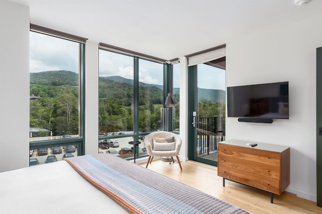 bedroom featuring access to outside, multiple windows, expansive windows, and light hardwood / wood-style floors