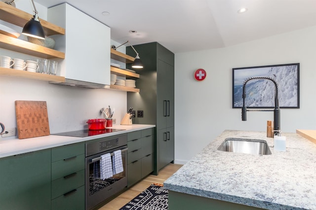 kitchen with stainless steel oven, black electric stovetop, sink, green cabinetry, and light wood-type flooring