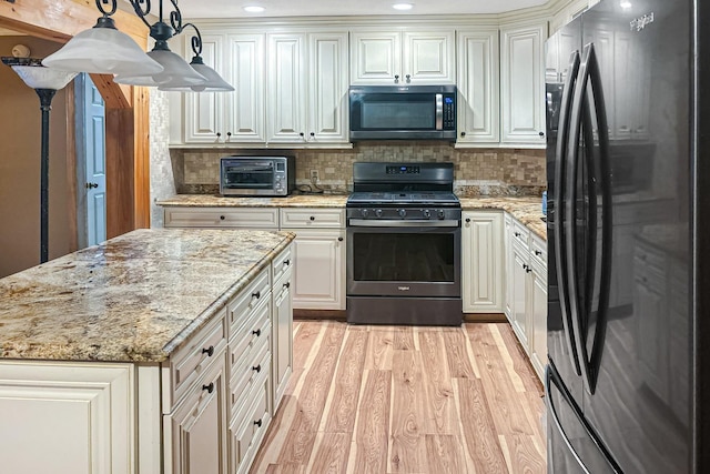 kitchen with light stone countertops, appliances with stainless steel finishes, light wood-type flooring, decorative backsplash, and pendant lighting