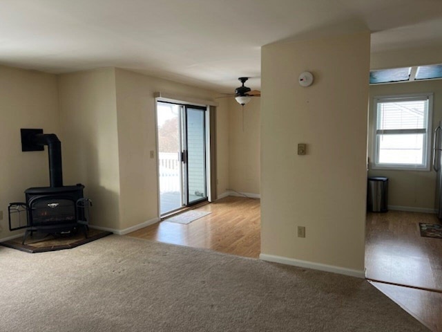 unfurnished living room with ceiling fan, light wood-type flooring, and a wood stove