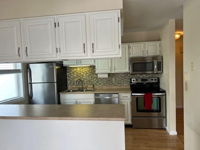 kitchen featuring appliances with stainless steel finishes, backsplash, sink, white cabinets, and hardwood / wood-style floors