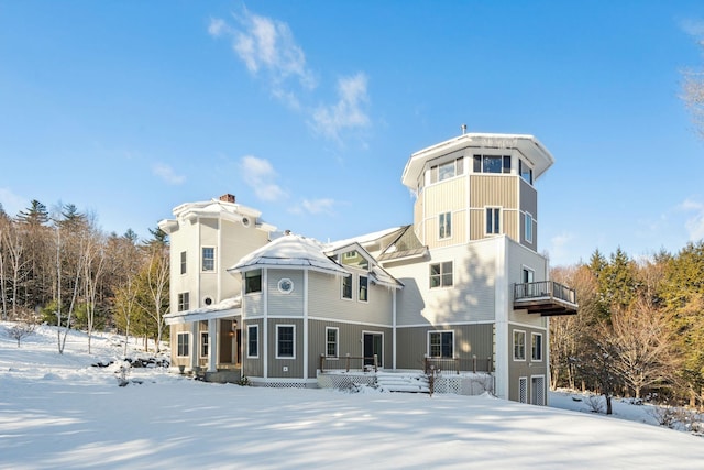 snow covered back of property featuring a balcony