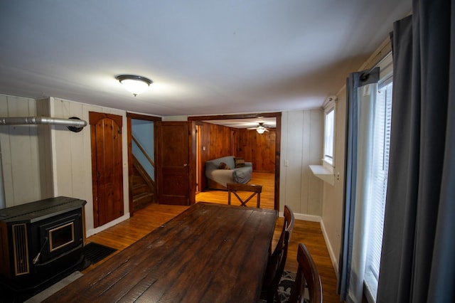 dining area with hardwood / wood-style floors, a wood stove, ceiling fan, and wooden walls