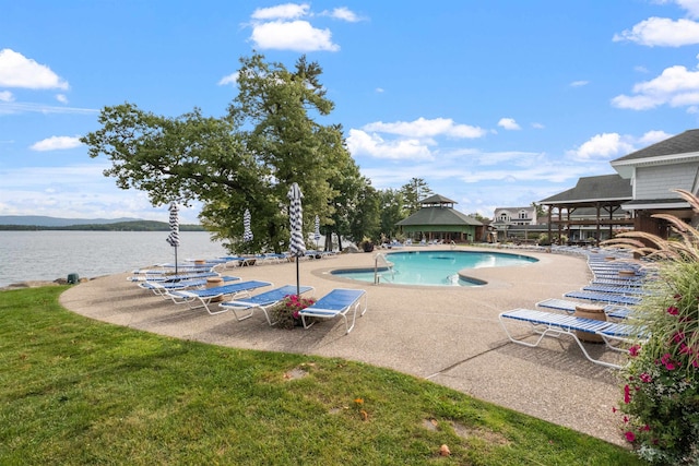 view of swimming pool featuring a lawn, a patio area, and a water view