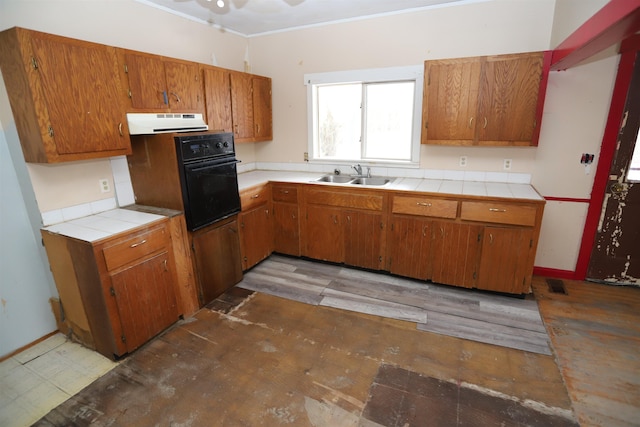 kitchen featuring ornamental molding, ceiling fan, sink, black oven, and tile counters