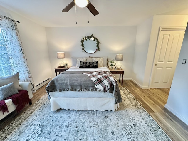 bedroom featuring a baseboard heating unit, ceiling fan, and light hardwood / wood-style flooring